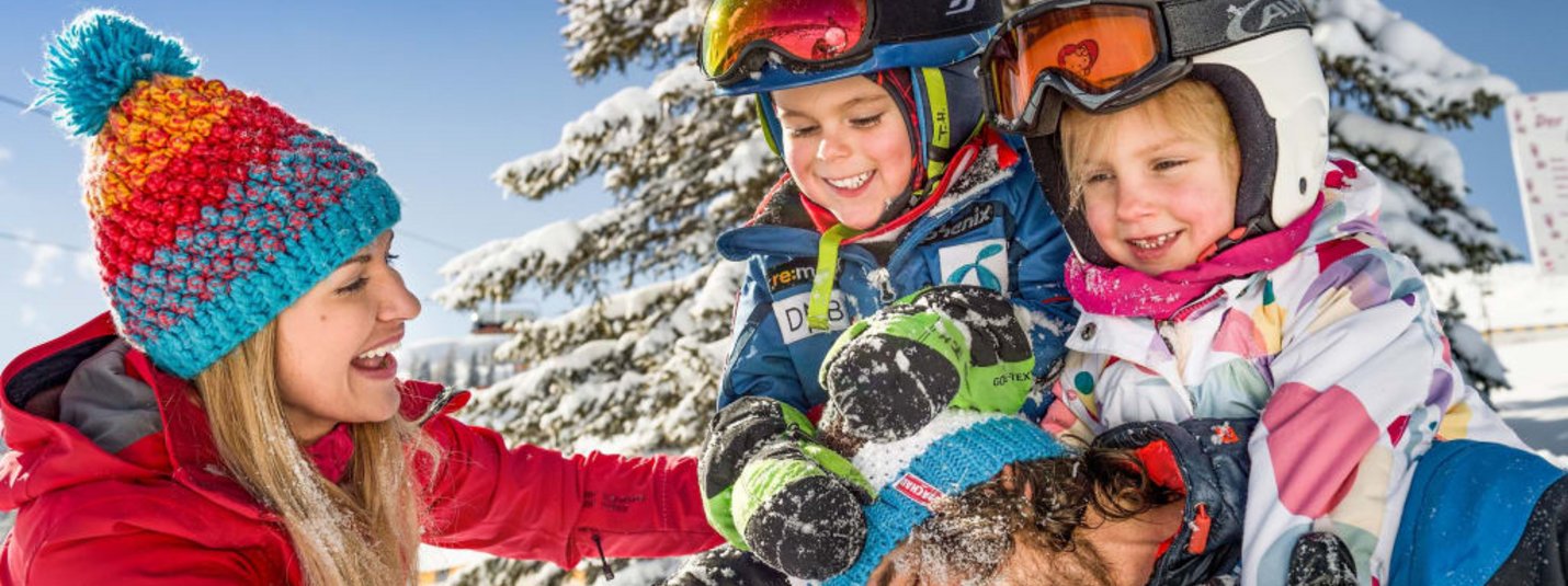 Familie spielt lachend im Schnee bei sonnigem Wintertag