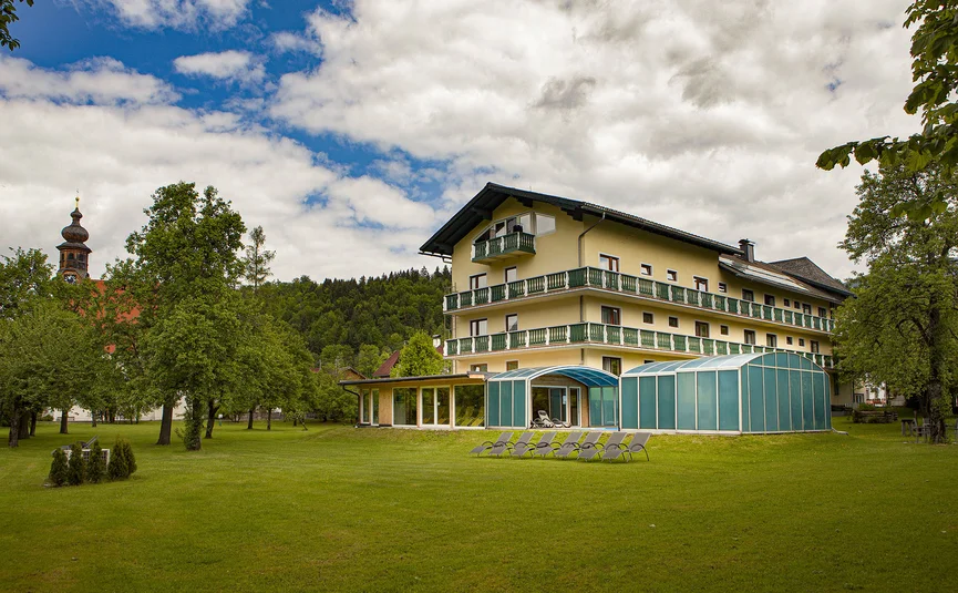 Geel hotelgebouw met zwembad en ligstoelen op groen gras