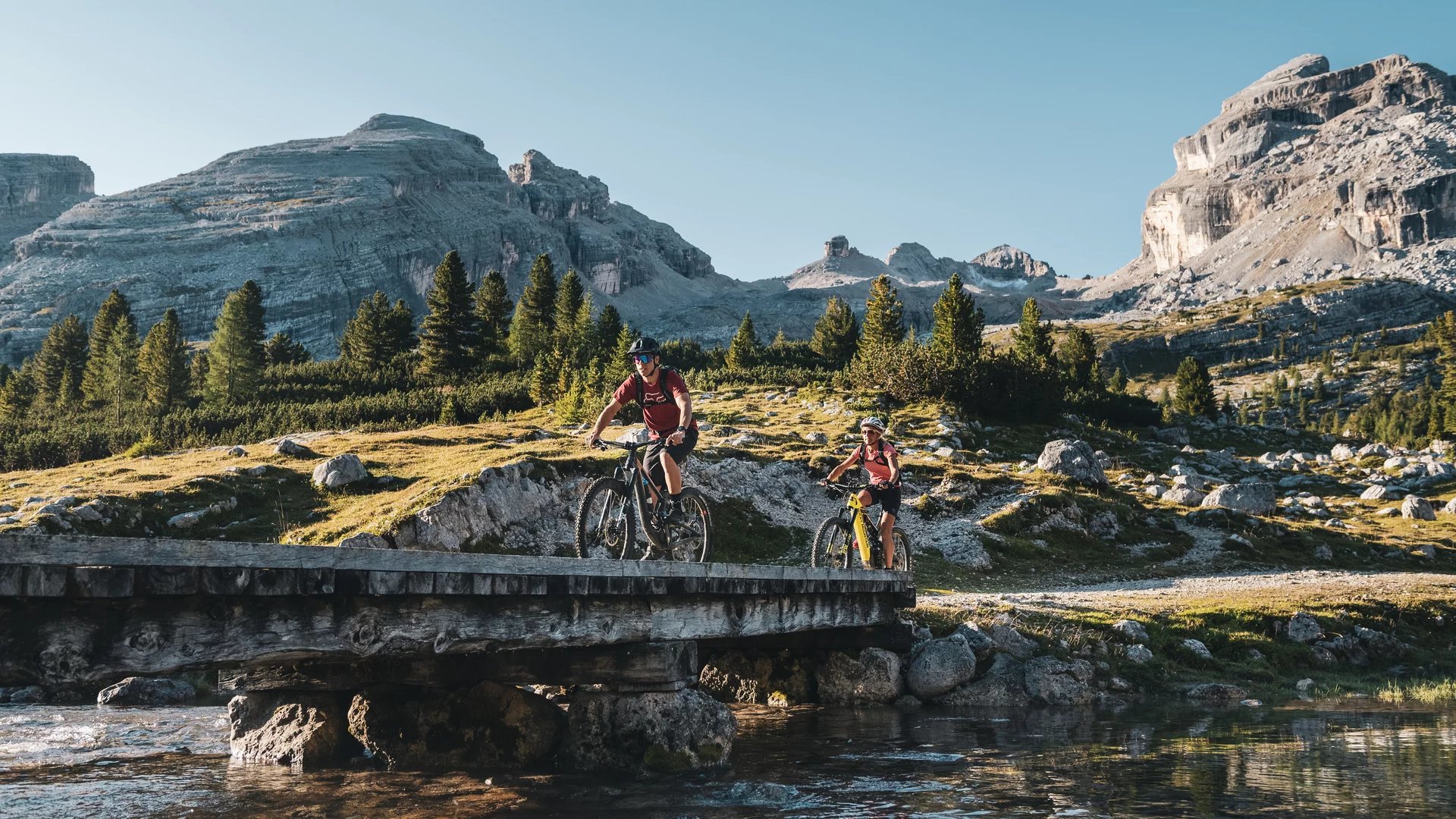 Dolomitenregion Kronplatz © Alex Moling Zwei Radfahrer fahren auf einer Brücke in den Bergen bei sonnigem Wetter