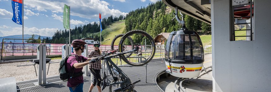 Zwei Radfahrer heben Mountainbikes zur Gondelstation in einer Berglandschaft