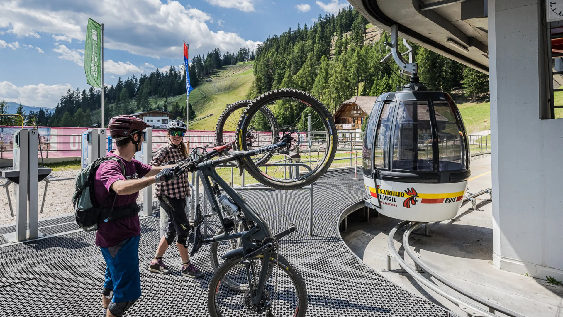 Zwei Radfahrer heben Mountainbikes zur Gondelstation in einer Berglandschaft