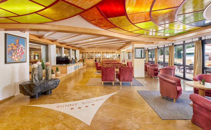 Bright hotel lobby with colorful ceiling mosaic and red armchairs
