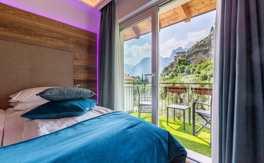 Hotel room with bed and balcony overlooking mountains and garden