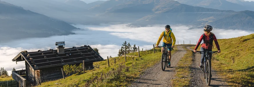 Mountainbike-Urlaub in Tirol © TVB Kitzbüheler Alpen Brixental - Mathäus Gartner Zwei Radfahrer fahren auf Bergweg mit Nebel im Tal und Bergen im Hintergrund