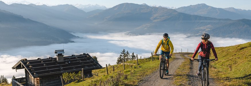 Lifesporthotel Hechenmoos *** © TVB Kitzbüheler Alpen Brixental - Mathäus Gartner Zwei Radfahrer fahren auf Bergweg mit Nebel im Tal und Bergen im Hintergrund
