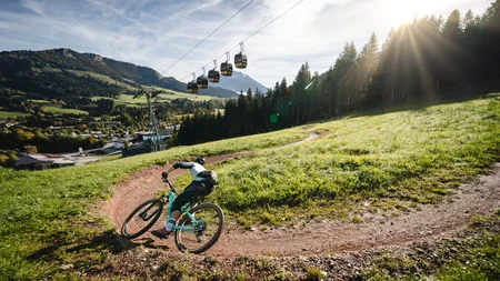 Mountainbiker fährt auf kurvigen Trail in sonniger Berglandschaft