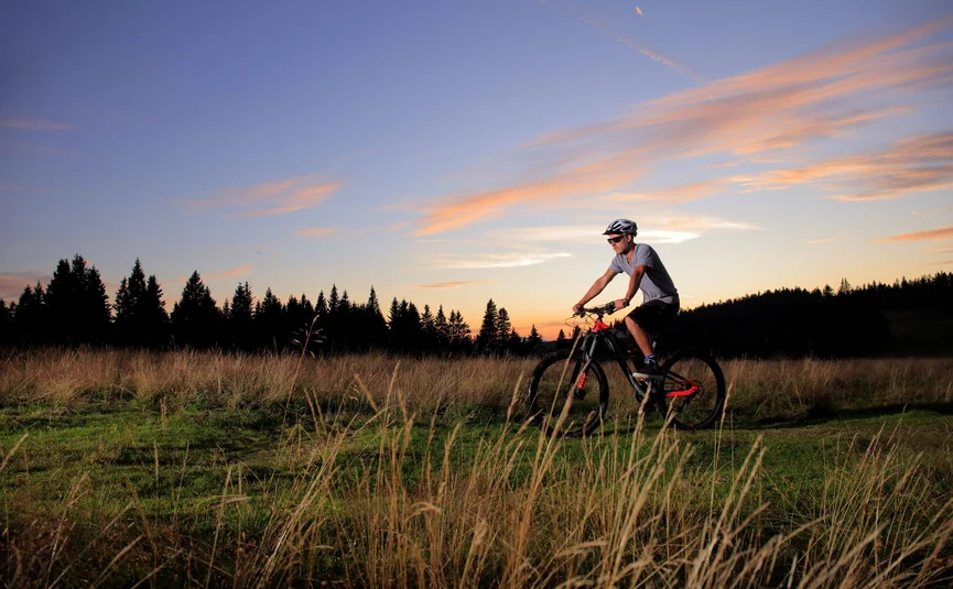Man mountainbiken op grasveld bij zonsondergang