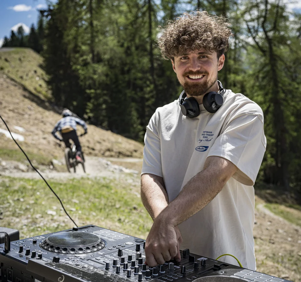 GREEN DAYS 2026 in Nauders-Reschensee
© Manfred Stromberg Lächelnder DJ mit Kopfhörern draußen vor Bäumen und Radfahrer im Hintergrund