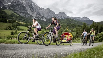 Familie fährt Fahrräder mit Kind im Fahrradanhänger in den Bergen