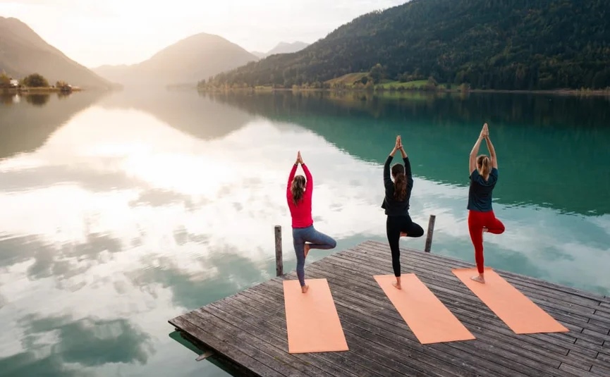 Natürlich Im Moment Drie vrouwen doen yoga op matten op een steiger bij een rustig bergmeer