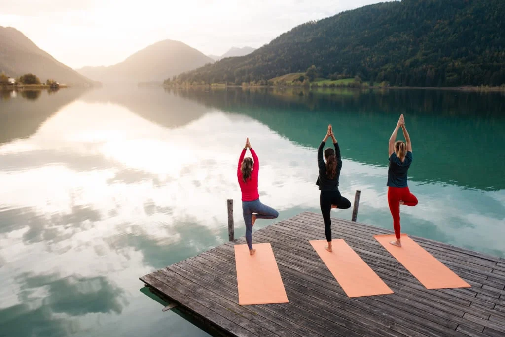 Drei Frauen machen Yoga auf einer Stegmatte am ruhigen Bergsee