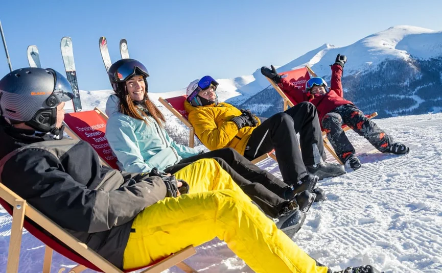 Easter Bunny Fun includes ski pass - 5 nights Four people in ski gear sit on sled chairs in snowy mountains