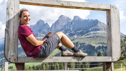 Between Rosengarten and Latemar: Mountain biking in the Dolomites’ most beautiful open-air cinema
© WOM Medien - Andreas Meyer Woman sitting on large wooden frame with alpine mountain view in background