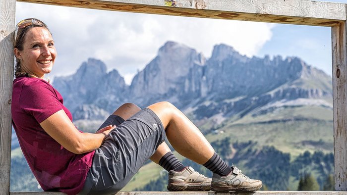 Bike und Hike – der alpine Trendsport, der das Beste aus zwei Welten vereint © WOM Medien - Andreas Meyer Frau sitzt auf großem Holzrahmen mit Alpenpanorama im Hintergrund