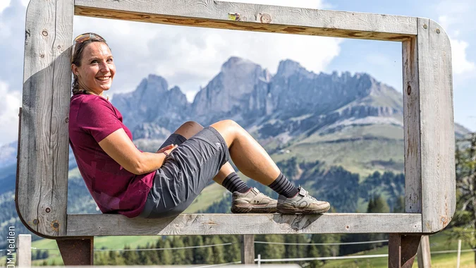 Mountain Bike Holidays © WOM Medien - Andreas Meyer Frau sitzt auf großem Holzrahmen mit Alpenpanorama im Hintergrund