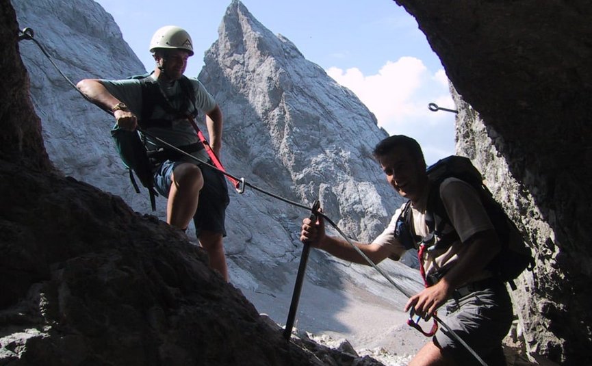 Two climbers with gear in a rock opening near a mountain peak