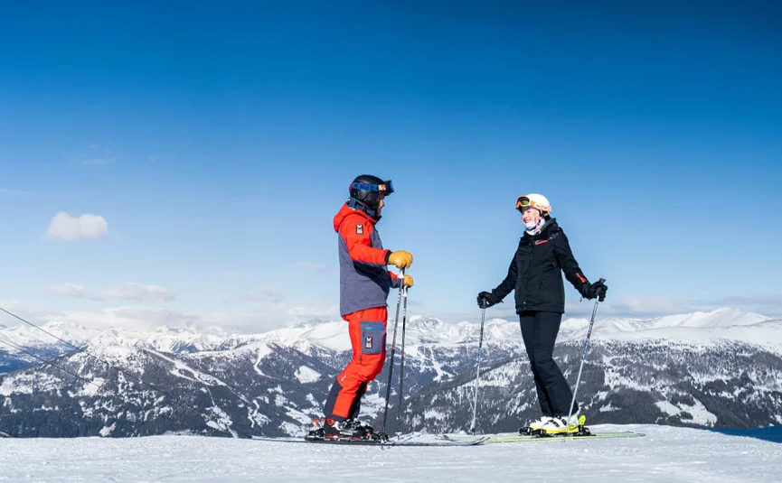 Ski & Wellness - 3 nights Two skiers in colorful outfits standing on snowy mountain with scenic view