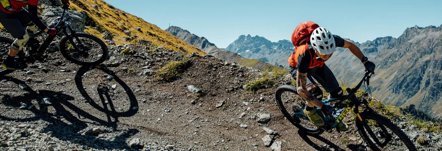 Zwei Mountainbiker fahren auf einem bergigen Pfad unter klarem Himmel