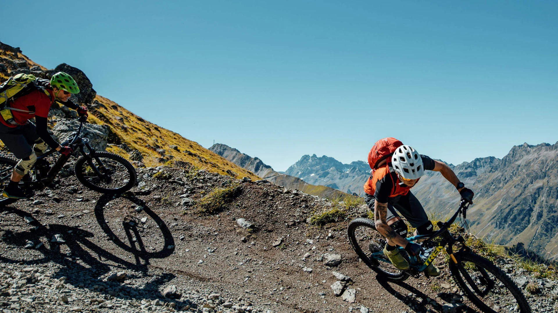 Zwei Mountainbiker fahren auf einem bergigen Pfad unter klarem Himmel