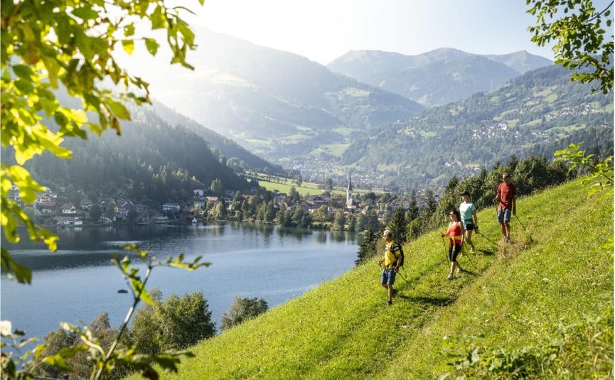 Hikers walking on green hillside with mountain and lake view