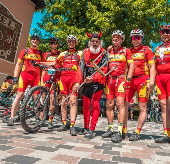 Seven cyclists in red jerseys and a man in devil costume in front of a hotel