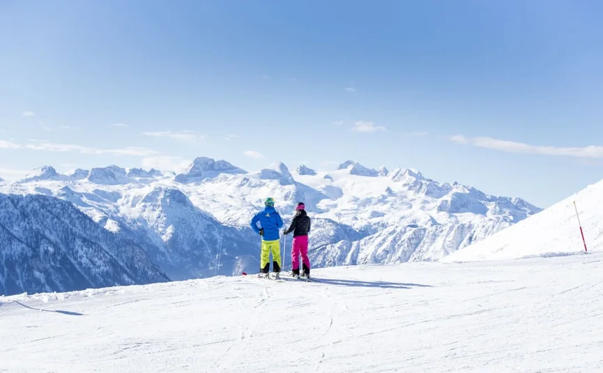 Ski Woche 7 Nächte inkl. Skipass Zwei Skifahrer blicken auf einer verschneiten Piste auf die Alpen