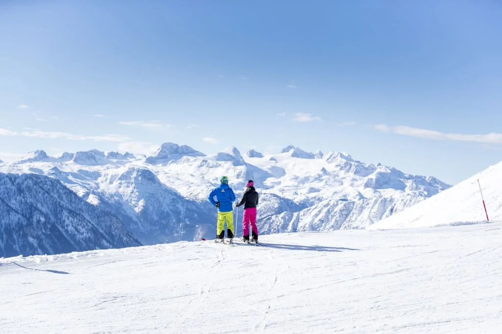 Ski Woche 7 Nächte inkl. Skipass Zwei Skifahrer blicken auf einer verschneiten Piste auf die Alpen