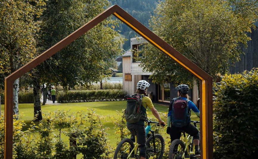 Zwei Radfahrer mit Helmen und Rucksäcken im Park neben einem See