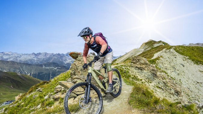 Mountainbiker fährt auf schmalem Bergpfad bei sonnigem Wetter