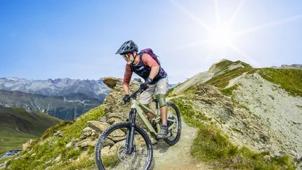 Mountainbiker fährt auf schmalem Bergpfad bei sonnigem Wetter