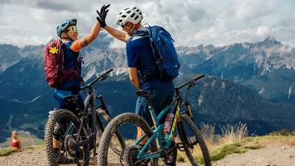 Zwei Mountainbiker geben sich auf einem Berggipfel abklatschend die Hand