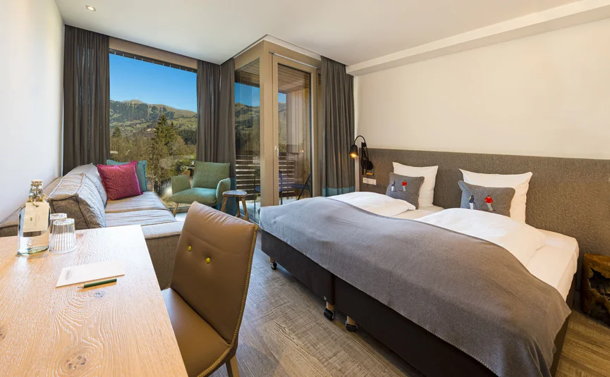 Helles Hotelzimmer mit Doppelbett, Sofa und Bergblick durch große Fenster