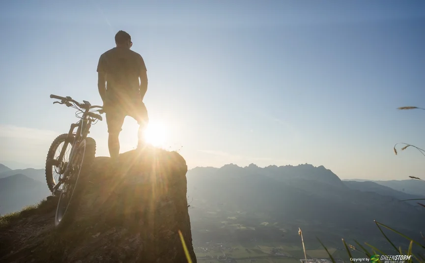 Man met fiets op bergtop bij zonsondergang
