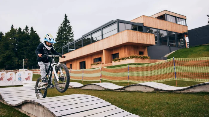 Child wearing helmet riding mountain bike over wooden roller track