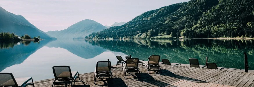 Liegestühle auf Holzsteg am ruhigen Bergsee mit Spiegelung der Berge
