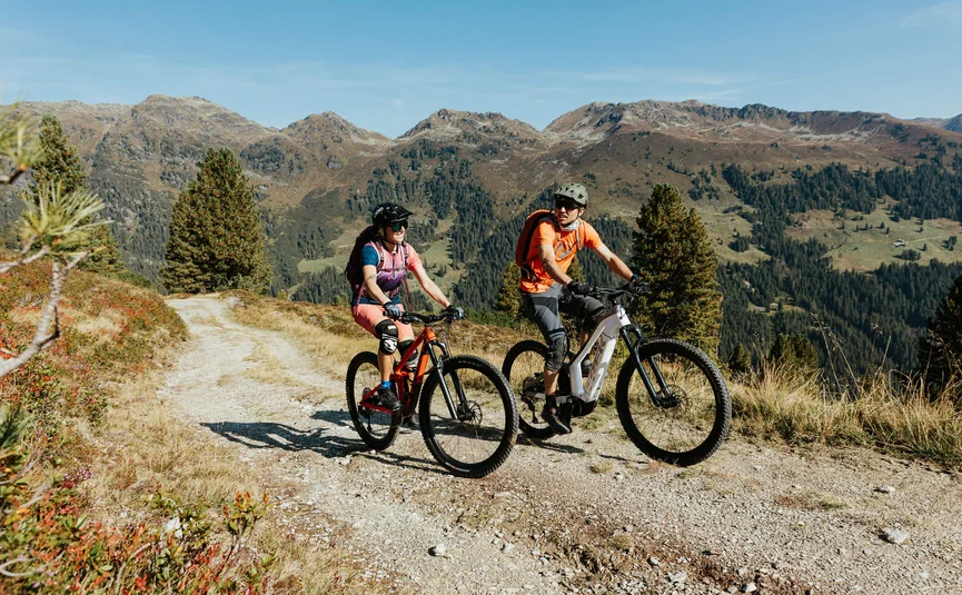 Zwei Radfahrer auf einem Bergweg mit Herbstlandschaft im Hintergrund