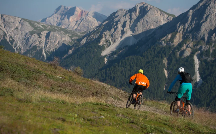 Zwei Mountainbiker fahren auf einem Bergpfad mit felsigen Bergen im Hintergrund