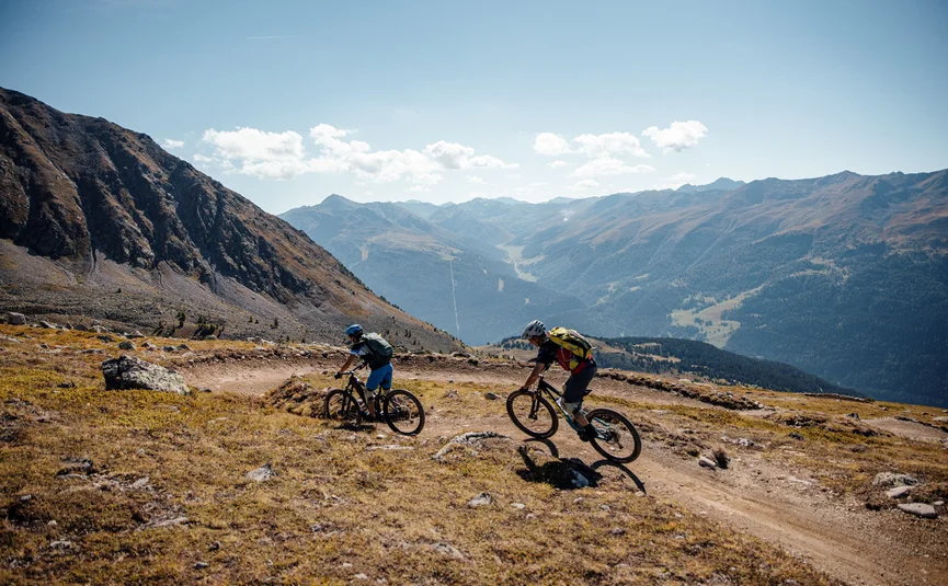 Two mountain bikers riding on a mountain trail with scenic mountain view