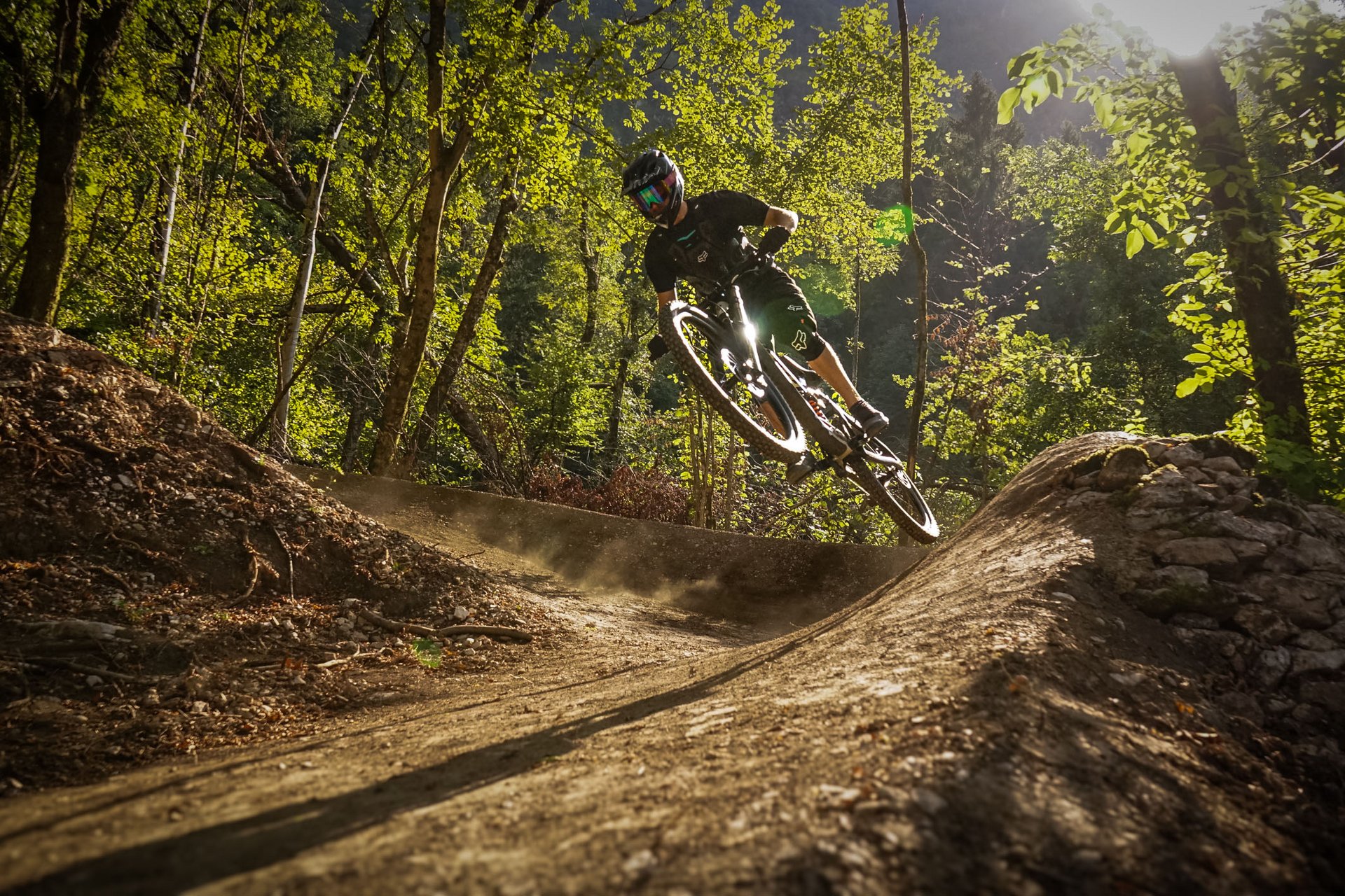 Mountainbiker springt auf Waldtrail im Sonnenlicht