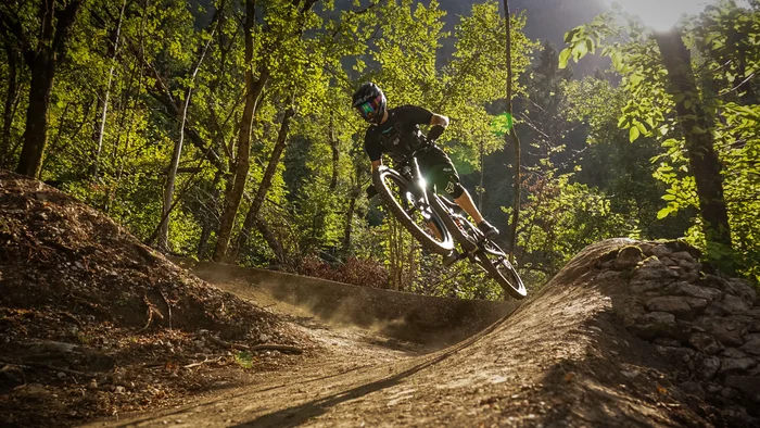 Mountainbiker springt auf Waldtrail im Sonnenlicht