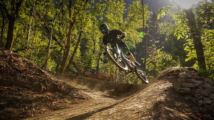 Airline © Bike Park Bovec Mountainbiker springt auf Waldtrail im Sonnenlicht