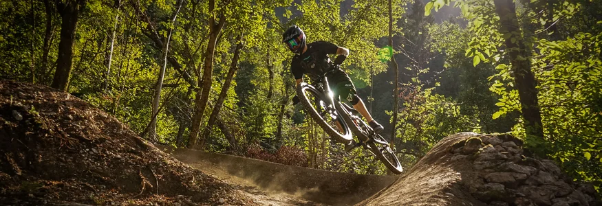 Dein Julische Alpen-Guide © Bike Park Bovec Mountainbiker springt auf Waldtrail im Sonnenlicht