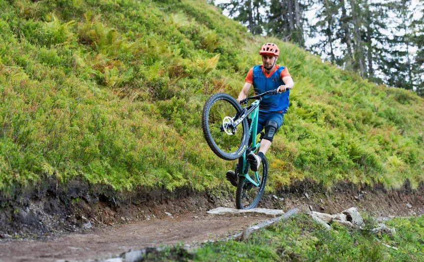 Man maakt een wheelie met mountainbike op bospad