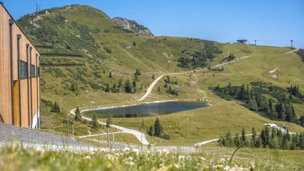 Grüner Berg mit See, Wanderwegen und Seilbahn unter klarem Himmel