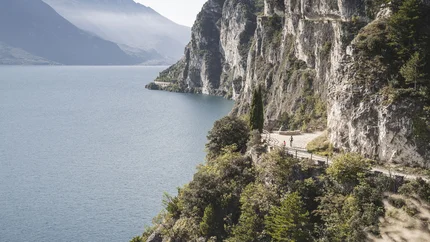 Fietsers op een bergpad langs een meer met steile kliffen en bos