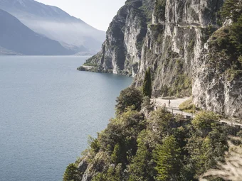Cyclists on a mountain path by a lake with steep cliffs and forest