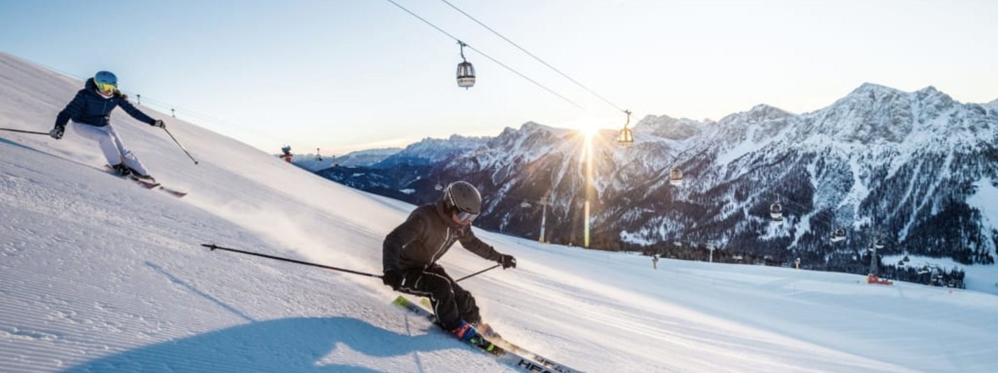 Dolomiti Super Première 8=6 Twee skiërs skiën op besneeuwde helling met kabelbanen en bergen op achtergrond