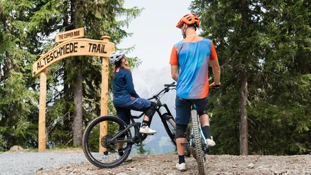 Unterwegs in Österreichs größter Bikeregion © Patrick Wasshuber Zwei Mountainbiker am Eingang des Altschmiede-Trails im Wald