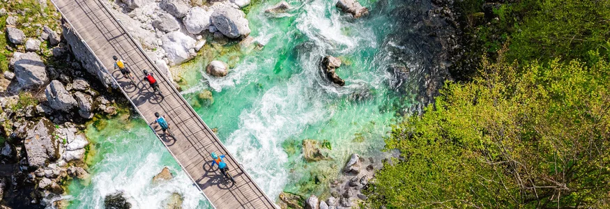 Dein Julische Alpen-Guide © Soca Valley - Ziga Koren Radfahrer überqueren eine Brücke über einen klaren, grünen Fluss