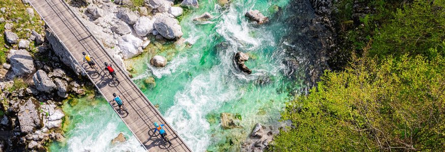 Radfahrer überqueren eine Brücke über einen klaren, grünen Fluss
